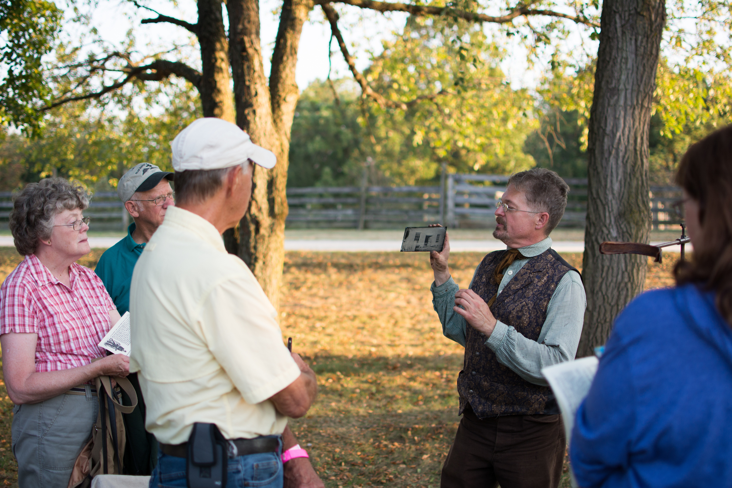  a group of older white people stand around a man in period costume (Dave Rambow) telling them about H.H. Bennett
